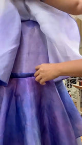 Person wearing a purple dress with a hand adjusting the fabric.