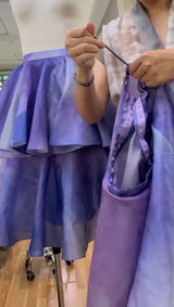 Person holding a purple skirt next to a mannequin wearing a similar skirt.