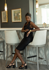 Woman in a black dress sitting on a bar stool in a modern kitchen.