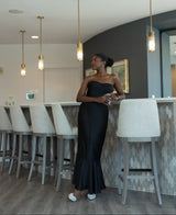 Woman in a black dress standing in a modern interior setting with pendant lights.