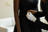 Person buttoning a black dress with gloved hands, blurred background