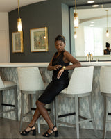 Woman in a black dress sitting on a bar stool in a modern kitchen.