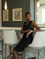 Woman in a black dress sitting at a bar counter with decor elements in the background