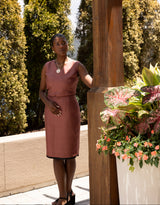 Woman in a pink dress standing next to a wooden post with plants in the background