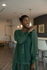 Woman in a green dress standing in a room with chairs and a table.