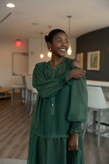 Woman in a green dress standing in a room with chairs and a table.