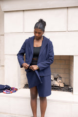 Woman in a blue suit standing in front of a white wall.