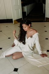 Woman in a white outfit sitting on a tiled floor.