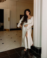 Woman in a white dress standing in a room with tiled floor and white walls.