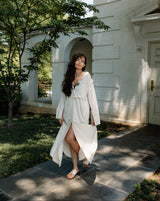 Woman in a white dress standing outside a building with trees and grass.